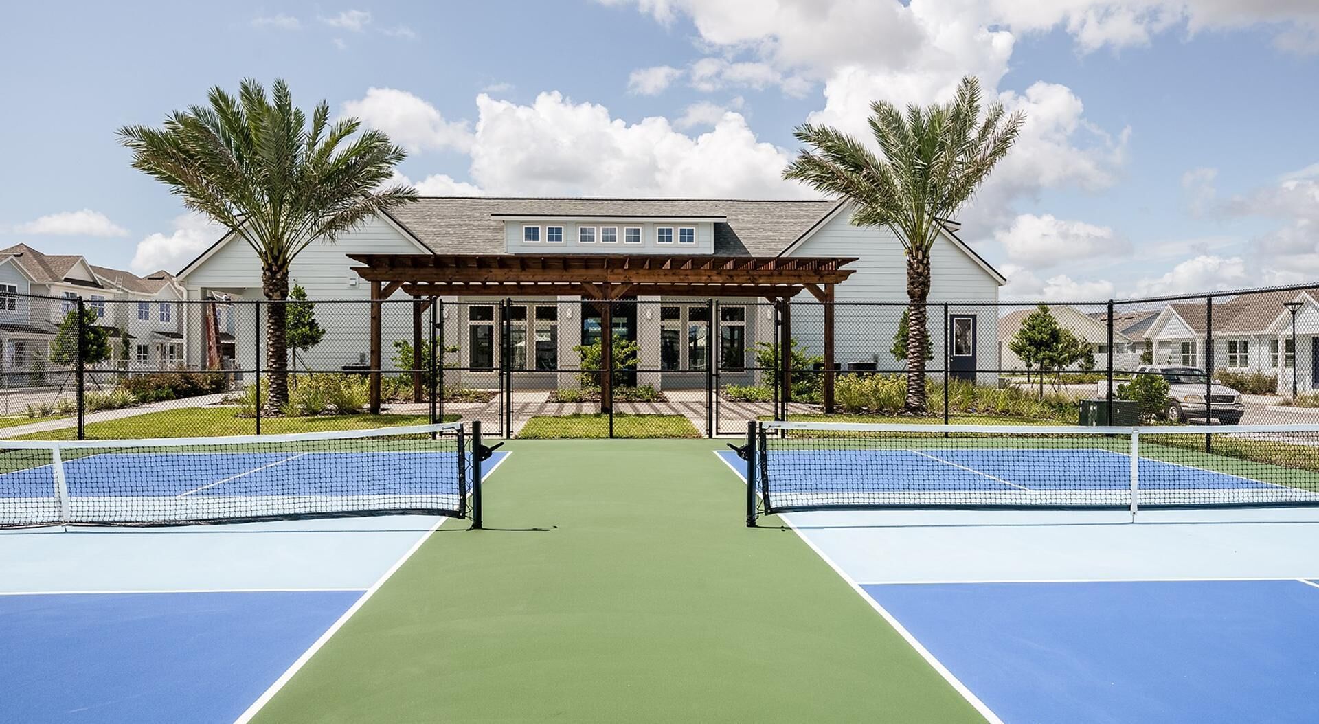 A tennis court with a wooden pavilion in the center, surrounded by residential buildings and palm trees.