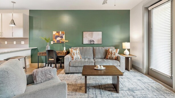 A living room with a grey sofa, a coffee table, and a dining area with a wooden table and chairs. - Landing | Incredible 1BD, Gym, Clubhouse (Charlotte)