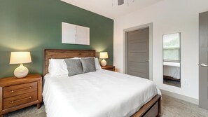 A bedroom with a bed, two bedside tables with lamps, a door, and a window with blinds. - Landing | Incredible 1BD, Gym, Clubhouse (Charlotte)