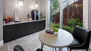 A modern kitchen with a coffee machine, a dining table with chairs, and a view of a brick wall and greenery outside. - Landing | Incredible 1BD, Gym, Clubhouse (Charlotte)