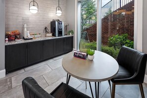 A modern kitchen with a coffee machine, a dining table with chairs, and a view of a brick wall and greenery outside. - Landing | Incredible 1BD, Gym, Clubhouse (Charlotte)