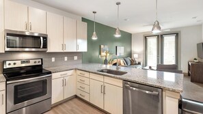 A modern kitchen with stainless steel appliances, light wood cabinets, a granite countertop, and pendant lighting. - Landing | Amazing 1BD, Gym, Clubhouse (Charlotte)