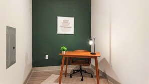 A room with a desk, chair, lamp, and a framed picture on the wall. - Landing | Modern 1BD, Gym, Yoga Studio (Charlotte)