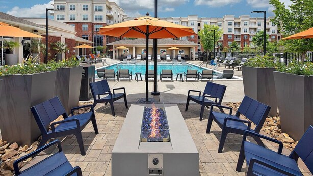 Ein Poolbereich mit Liegestühlen, einem Feuerelement und Sonnenschirmen.