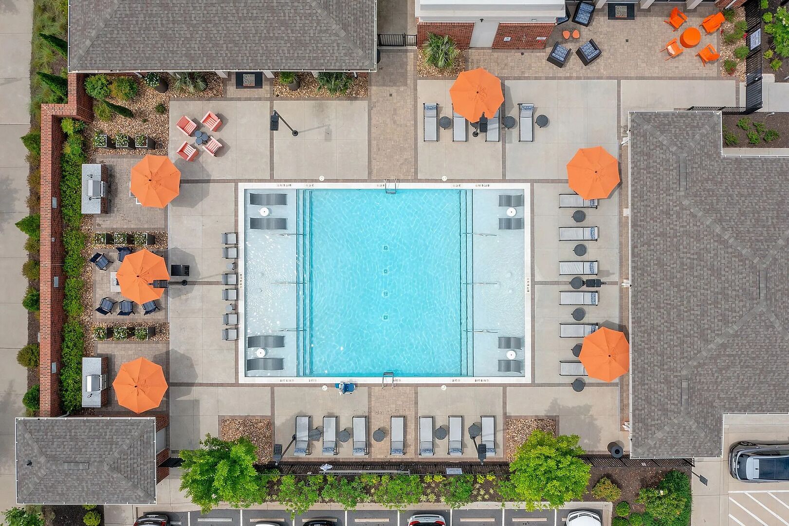 Vista aérea de una zona de piscina con tumbonas y sombrillas, rodeada de senderos de ladrillo y vegetación.