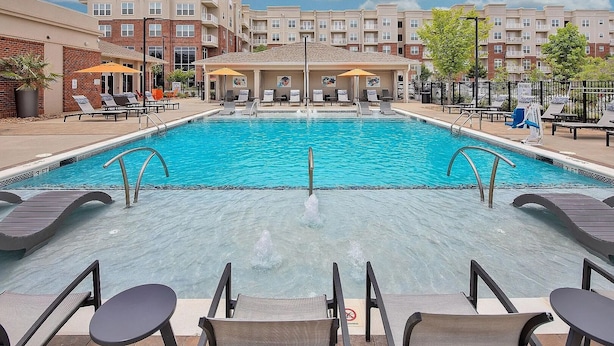 A swimming pool with lounge chairs and umbrellas, surrounded by multi-story buildings. - Landing | Incredible 1BD, Gym, Yoga Studio (Charlotte)