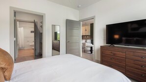 A bedroom with a bed, a TV, a dresser, and a mirror. - Landing | Incredible 1BD, Gym, Yoga Studio (Charlotte)