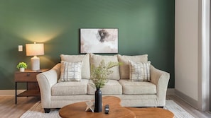 A living room with a sofa, a coffee table, a lamp, a vase with flowers, and a painting on the wall.