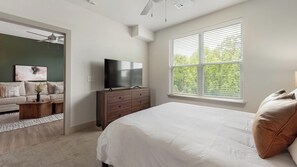 A bedroom with a bed, a dresser, a television, and a window with blinds.
