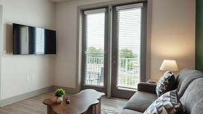 Ein Wohnzimmer mit Flachbildfernseher, einer Couch, einem Couchtisch mit Pflanze und einer Lampe.