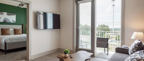Ein modernes Hotelzimmer mit Bett, Flachbildfernseher, Balkon mit Blick und einer Sitzecke mit Lampe.