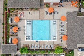 An aerial view of a swimming pool area with sun loungers and umbrellas, surrounded by brick pathways and greenery. - Landing | Chic 1BD, Gym, Yoga Studio (Charlotte)