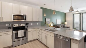 A modern kitchen with stainless steel appliances, a granite countertop, and a view to the living area. - Landing | Stylish 1BD, Gym, Yoga Studio (Charlotte)