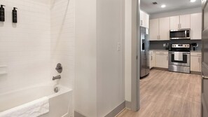 A modern kitchen with stainless steel appliances, a wooden floor, and light-colored cabinetry. - Landing | Stylish 1BD, Gym, Yoga Studio (Charlotte)