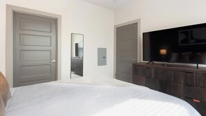 Una habitación de hotel con una cama, un televisor sobre una cómoda de madera y una puerta que da a otra habitación.