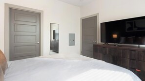 A hotel room with a bed, a TV on a wooden dresser, and a door leading to another room. - Landing | Amazing 1BD, Gym, Clubhouse (Charlotte)