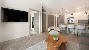 A modern living room with a flat-screen TV, a wooden coffee table with a plant, and a grey sofa. - Landing | Stylish 1BD, Gym, Yoga Studio (Charlotte)