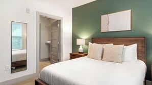 Quarto de hotel com uma cama, uma mesa de cabeceira com abajur, uma porta que dá para um armário e um quadro na parede.