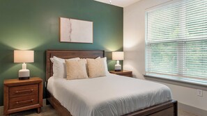A bedroom with a bed, two bedside tables, a nightstand, a window with blinds, and a wall-mounted artwork. - Landing | Amazing 1BD, Gym, Clubhouse (Charlotte)