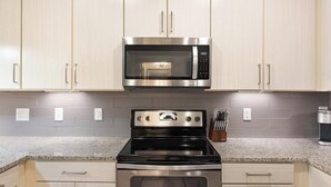 Uma cozinha com armários de madeira clara, micro-ondas de aço inoxidável e fogão preto.