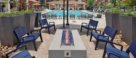 Un área junto a la piscina con sillones, una chimenea y sombrillas.