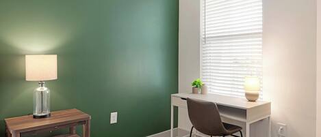 A room with a desk, chair, lamp, and a window with blinds.