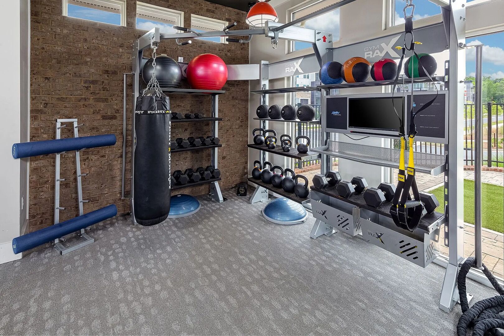 Ein Fitnessstudio mit Backsteinwand, verschiedenen Trainingsgeräten und einem Fernsehbildschirm.