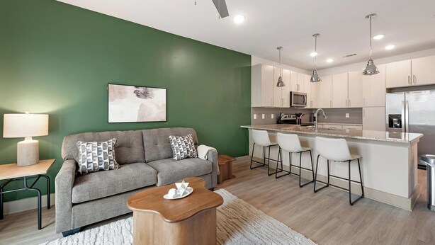 Un salon moderne avec un canapé gris, une table basse en bois et un mur d’accent vert.