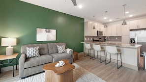 A modern living room with a grey sofa, a wooden coffee table, and a green accent wall. - Landing | Stylish 1BD, Clubhouse, Yoga Studio (Charlotte)