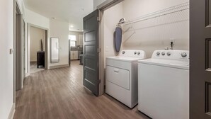 A laundry area with a washing machine and dryer, a drying rack, and a hallway leading to a kitchen. - Landing | Stylish 2BD, Clubhouse, Gym (Charlotte)