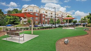 A landscaped outdoor area with artificial grass, two wooden benches, and red umbrellas. - Landing | Stylish 2BD, Clubhouse, Gym (Charlotte)