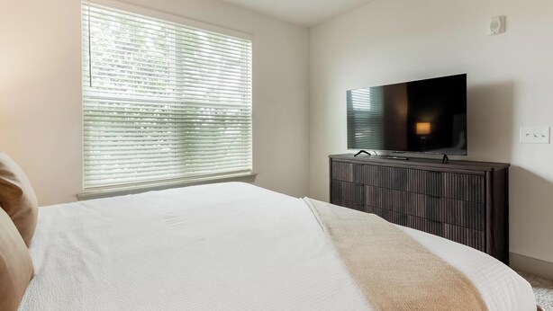 A bedroom with a bed, a dresser, a television, and a window with blinds. - Landing | Stylish 2BD, Clubhouse, Gym (Charlotte)