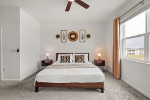 A bedroom with a wooden bed, two bedside tables with lamps, a ceiling fan, and a large window with curtains. - 3 BD/ 2 BA/ Champions Gate (1005 SS) (Davenport)