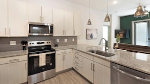 A modern kitchen with stainless steel appliances, light wood cabinetry, a granite countertop, and pendant lighting. - Landing | Chic 2BD, Gym, Yoga Studio (Charlotte)
