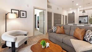 A modern living room with a grey sofa, a white armchair, and a wooden coffee table with a plant. - Landing | Chic 2BD, Gym, Yoga Studio (Charlotte)