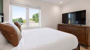 Un dormitorio con una cama grande, un aparador de madera, un televisor de pantalla plana y una ventana con persianas.