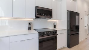 Eine moderne Küche mit weißen Schränken, einem Backofen, einem Kochfeld und einem schwarzen Kühlschrank.