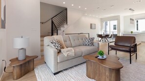 Ein modernes Wohnzimmer mit einer Couch, einem Couchtisch, einem Sessel und einer Treppe, die in eine obere Ebene führt.