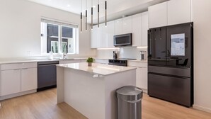 A modern kitchen with a central island, stainless steel appliances, and a window with blinds. - Landing | Stylish 3BD in Dallas (Dallas)