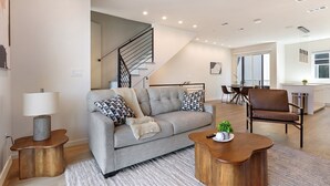 A modern living room with a grey sofa, patterned cushions, a wooden coffee table, and a staircase leading to an upper floor. - Landing | Spectacular 3BD in Dallas (Dallas)