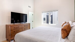 Ein Schlafzimmer mit einem Bett, einem Holzkapuzenmobel, einem Fernseher und einem Fenster mit Jalousien.