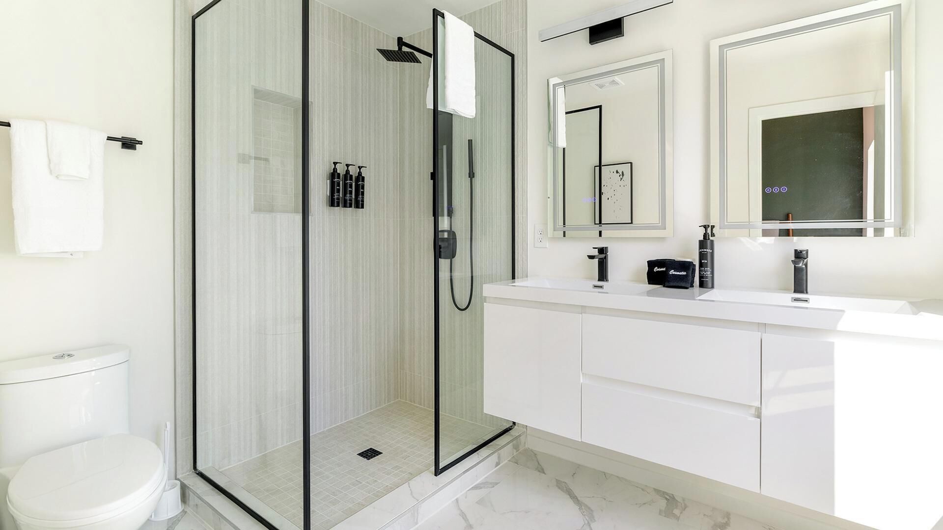 A modern bathroom with a glass-enclosed shower, a white vanity with a mirror, and a toilet.