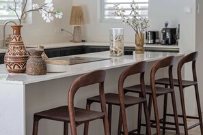 A kitchen island with a white countertop, three wooden bar stools, and decorative vases with flowers. - Villa Mira Alma full house Contemporary Luxury Villa in the Heart of Jan Thiel (Jan Thiel)