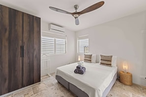 Ein Schlafzimmer mit einem Bett, einem Deckenventilator, einer Klimaanlage und einem Fenster mit Jalousien.
