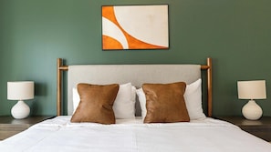 Ein Hotelzimmer mit einem Bett, zwei Nachttischen und einem an der Wand hängenden abstrakten Gemälde.