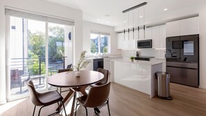 Eine moderne Küche mit weißen Schränken, einem Edelstahl-Kühlschrank und einem Essbereich mit rundem Tisch und Stühlen.