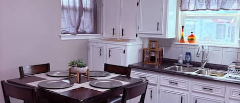 A kitchen with white cabinets, a dining table with chairs, a window with curtains, and a sink.