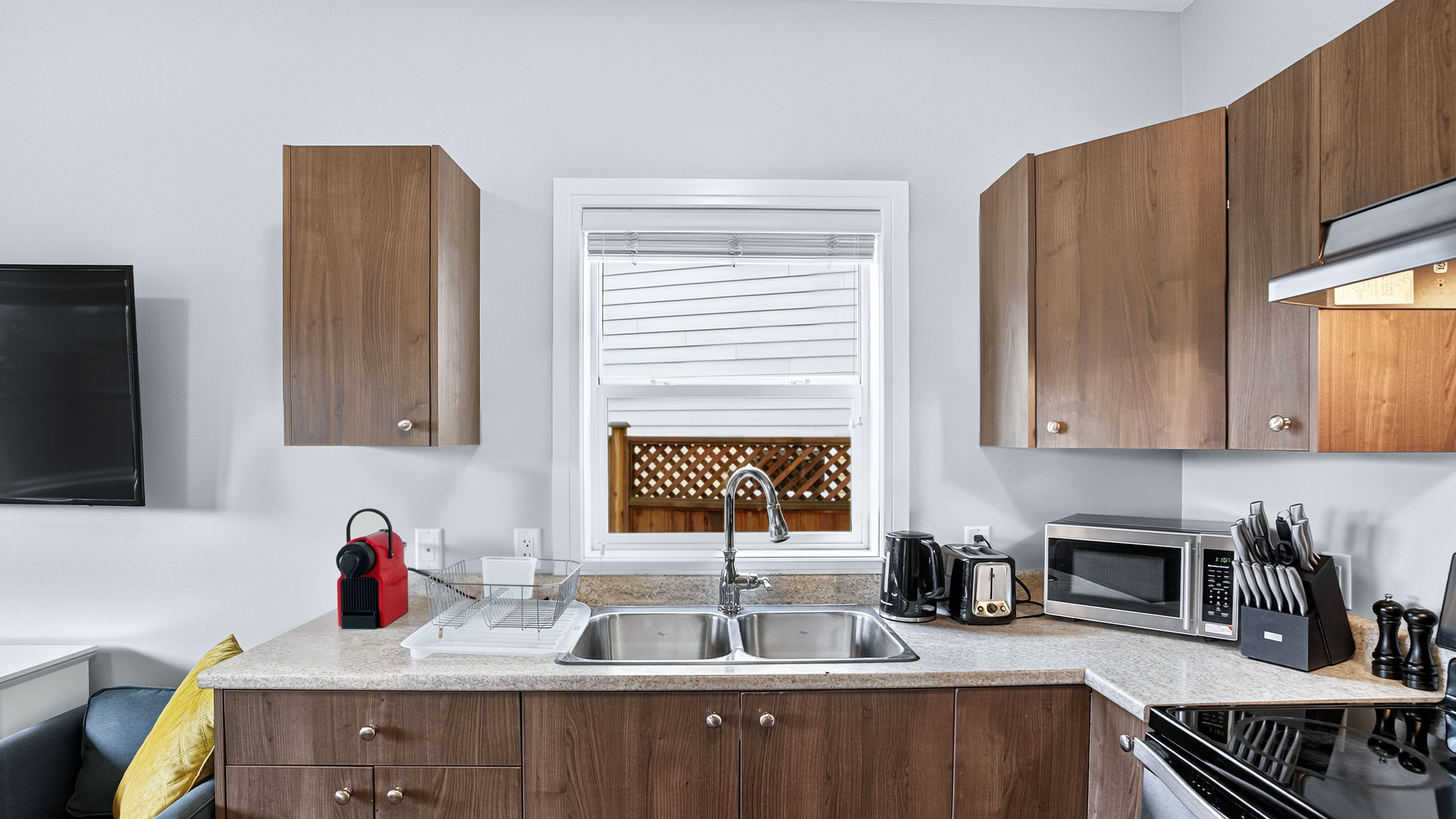 A modern kitchen with wooden cabinets, a double sink, a microwave, and a toaster.