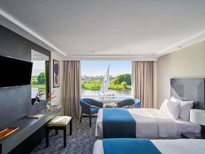 Hotelkamer met een bed, een bureau, een stoel, een televisie en uitzicht op een rivier en groen.