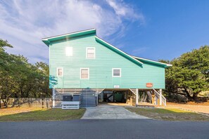 A two-story building with a sloped roof, a covered entrance, and a fenced area with a paved driveway leading to the entrance. - Newly Renovated Family Home in Ocean Sands (Corolla)